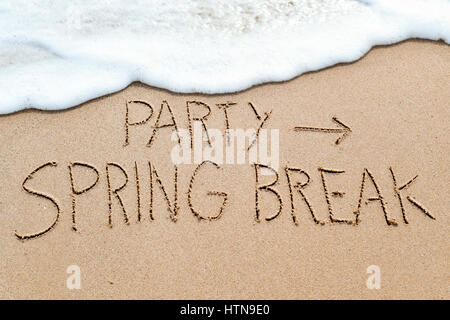 closeup of an arrow sign and the text party spring break written in the wet sand of the seashore, in a beach Stock Photo