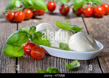 Three mozzarella cheese balls in a white bowl, garnished with cherry tomatoes and basil Stock Photo