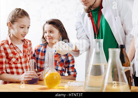 Getting interested. Pretty cute curious girl standing near the table and looking at the scientists hand while being interested in science Stock Photo