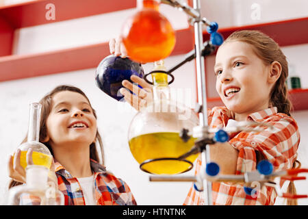 School scientific club. Cute joyful nice girls using scientific equipment and carrying out an experiment while being in the school lab Stock Photo