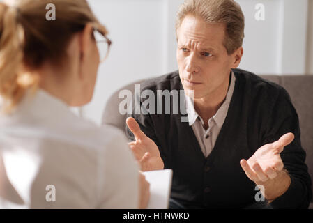 Constant stress. Sad miserable unhappy man looking at his therapist and telling her his story while suffering from stress Stock Photo