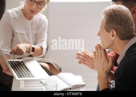 Working with colleagues. Nice pleasant positive man sitting with his colleagues and discussing a project while working at the office Stock Photo