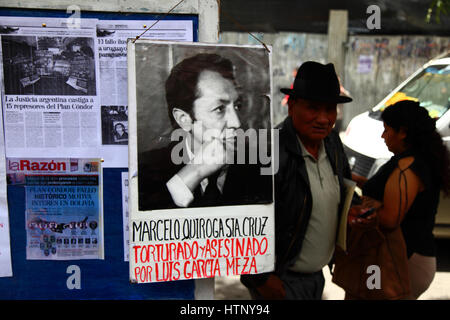 La Paz, Bolivia, 13th March 2017. People walk past a board with information about events during Bolivia's military dictatorships and Plan Condor. Today victims of the dictatorships commemorate 5 years of protests demanding justice and compensation for those that suffered, and that the government releases files from the period to help establish the truth about what happened. Marcelo Quiroga Santa Cruz was a writer and politician who was abducted during the coup of July 17 1980 and later murdered. Credit: James Brunker/Alamy Live News Stock Photo