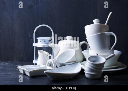Set of new white dishes with teapot, tea cups, and plates on a black wooden table Stock Photo