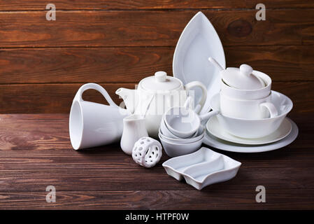 Set of new white dishes with teapot, tea cups, and plates on wooden table Stock Photo