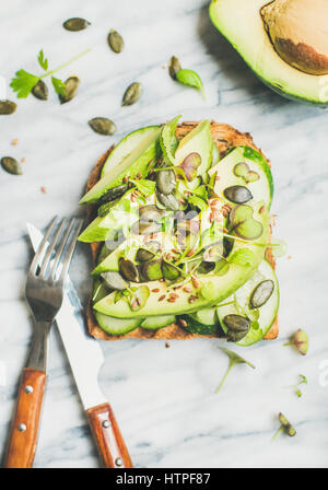 Healthy green veggie breakfast concept. Sandwich with avocado, cucumber, kale, kress sprouts, pumpkin seeds over marble background, top view. Vegan, w Stock Photo