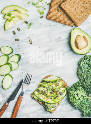 Healthy green veggie breakfast concept. Sandwich with avocado, cucumber, kale, kress sprouts and pumpkin seeds over marble background, top view, copy Stock Photo
