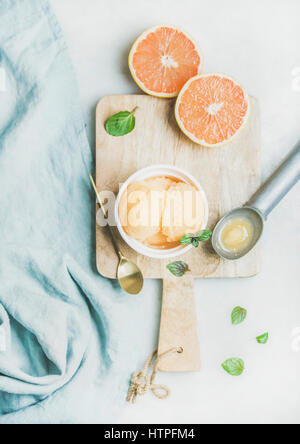 Pink grapefruit homemade sorbet with fresh mint leaves in white bowl on wooden board over light grey background, top view. Fresh healthy raw vegan sum Stock Photo