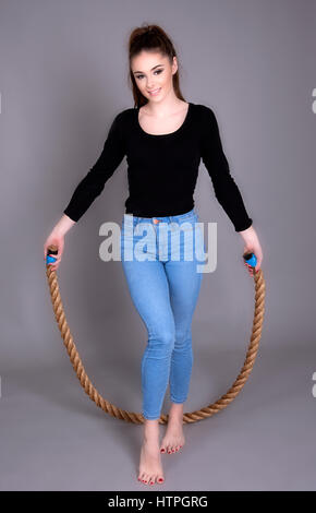 Young woman wearing jeans and a black top skipping with a thick rope Stock Photo