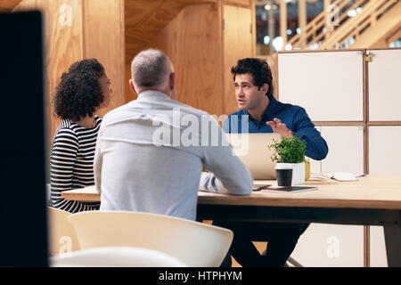 Focused young businessman having a meeting with two colleagues while sitting at a desk in a modern office using a laptop Stock Photo