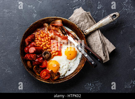 English Breakfast in cooking pan with fried eggs, sausages, bacon and beans on dark stone background copy space Stock Photo