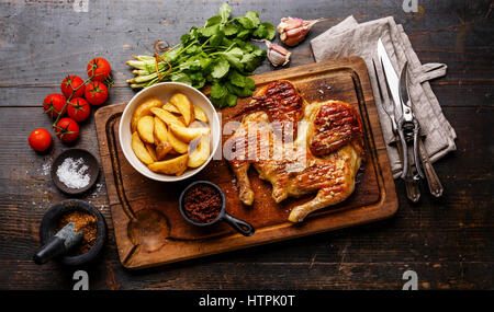 Grilled fried roast Chicken Tabaka and Potato wedges on cutting board on wooden background Stock Photo