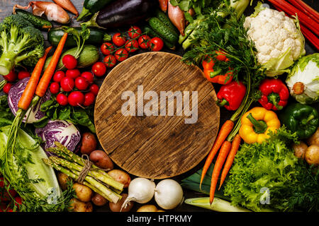 Fresh vegetables around round wooden cutting board copy space Stock Photo