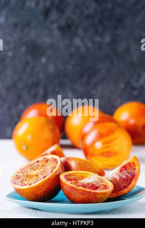 Sliced and whole ripe juicy Sicilian Blood oranges fruits on ceramic plate over white and gray concrete texture background. Copy space Stock Photo