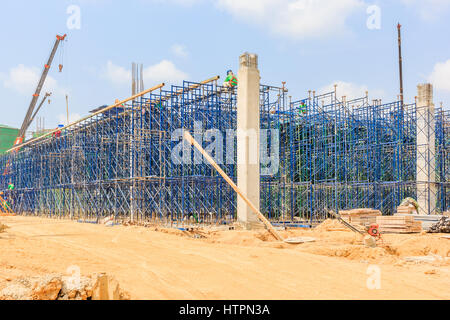 Construction workers wearing safety harness and installing scaffolding at high level in the construction site. Stock Photo
