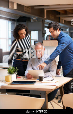 Diverse group of casually dressed professional colleagues talking business together over a digital tablet while having a meeting at a desk in a modern Stock Photo