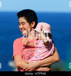 Smiling Asian male carrying his baby daugher Stock Photo