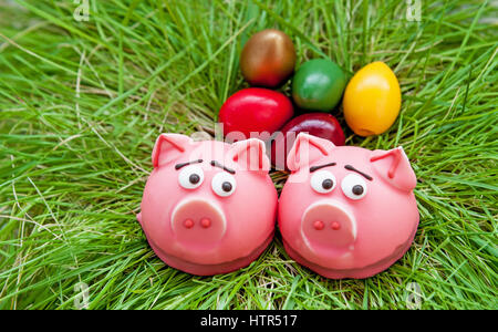 Easter composition of two baked sweet pig in a pink frosting in the nest of green grass with colored eggs Stock Photo
