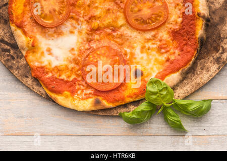 Feshly made wood fired pizza on pizza stone viewed from above on rustic grey boards Stock Photo