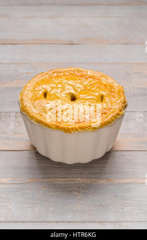 Deep sided individual pie in white ceramic dish on grey wooden boards Stock Photo