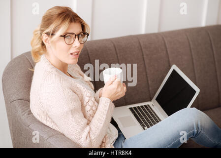 Taking a break. Hard working thoughtful nice woman sitting on the sofa and having tea while taking break from her work Stock Photo