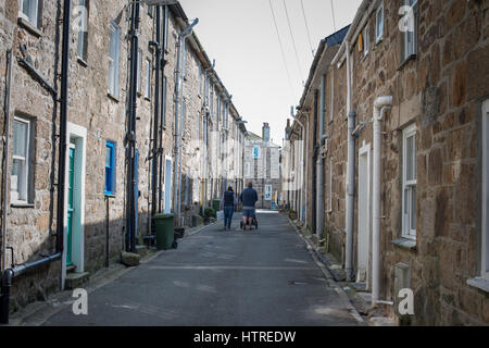 A man and women walk down a street past terraced houses in the town of St Ives, Cornwall, UK. Stock Photo