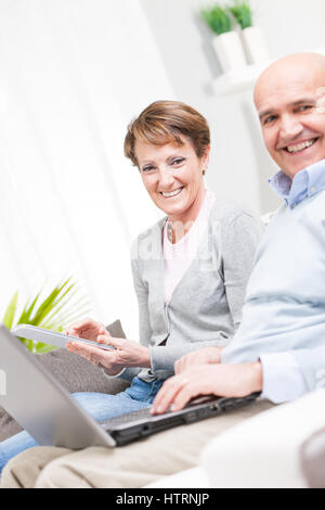 Happy couple relaxing with a laptop and tablet on a sofa at home with focus to the smiling attractive wife Stock Photo