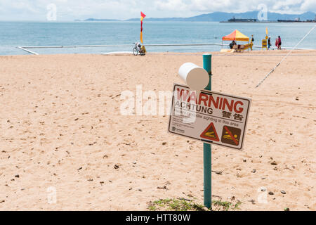 Warning sign for crocodile sighting on The Strand beach, Townsville, Australia with swimming nets in background Stock Photo