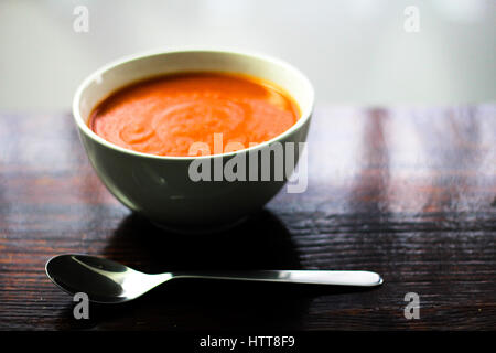 Picture of a bawl of tomato soup with a spoon on the side sitting on a wooden board Stock Photo
