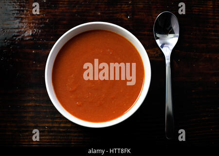 Picture of a bawl of tomato soup with a spoon on the side sitting on a wooden board Stock Photo