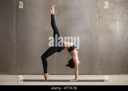 Young woman standing in One legged Wheel pose, grey studio Stock Photo