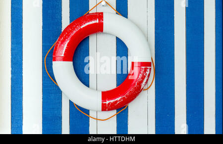RED AND WHITE LIFEBUOY ON BLUE AND WHITE STRIPED BACKGROUND Stock Photo