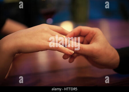 Young man makes woman marriage proposal and puts an engagement ring on her finger. Close up. They are sitting at table. Stock Photo