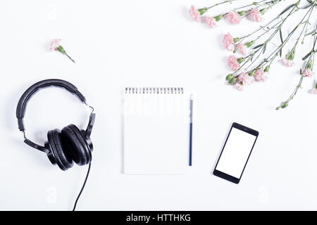 Top view of smart phone, headphones, paper notebook, pencil and flowers lie on white table Stock Photo