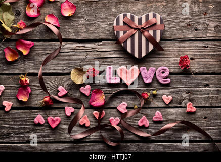 Word Love with heart shaped Valentines Day gift box on old vintage wooden plates. Sweet holiday background with rose petals, small hearts, curved ribb Stock Photo