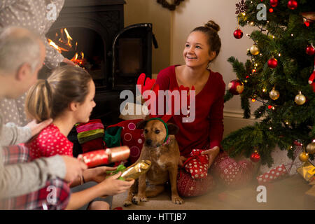 Family opening presents on Christmas morning. A girl is sitting with their dog who is wearing antlers. Stock Photo