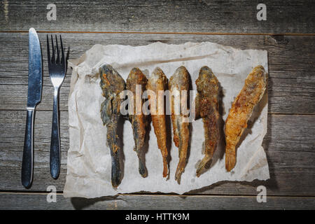 Dried fish with fork and knife on the table. Salty dry river fish on a wooden impressive background. Stock Photo