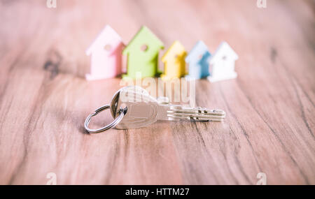 Silver Keychain laying on wooden Surface in front of miniature symbol of various coloured houses Stock Photo