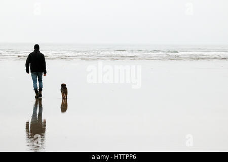 Man and his old Border Terrier dog walking along the beach in North Wales