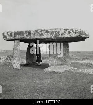 1950s, historical, woman stands under ancient stone structure or dolmen, Lanyon Quoit, Morvah. Cornwall, England. Stock Photo