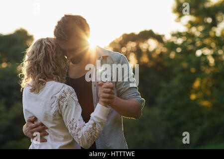 Affectionate young couple dancing hand in hand together while enjoying a romantic moment on sunny summer afternoon in a park Stock Photo