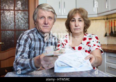 Russian male and female retirement people stretching bills and money in hands, sitting at the kitchen table Stock Photo