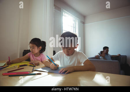 Boy and girl drawing in paper while parents using laptop in background Stock Photo
