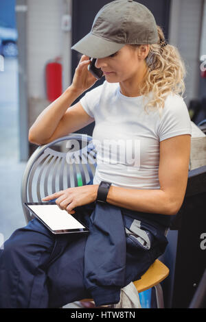 Female mechanic using digital tablet while talking on mobile phone Stock Photo