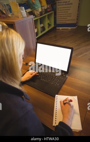 Woman using laptop and writing on notepad Stock Photo - Alamy