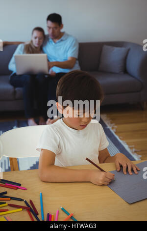 Attentive boy drawing in paper while his parents using laptop in background Stock Photo