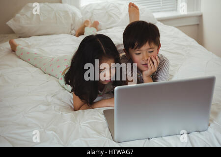 Siblings using laptop in bedroom Stock Photo