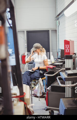 Female mechanic using digital tablet while talking on mobile phone Stock Photo