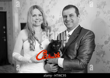 Happy and smiling Caucasian couple holding red word Family in russian in hands and black cat, grayscale image Stock Photo
