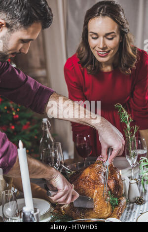 Young woman looking at husband carving the roasted turkey for Christmas dinner Stock Photo